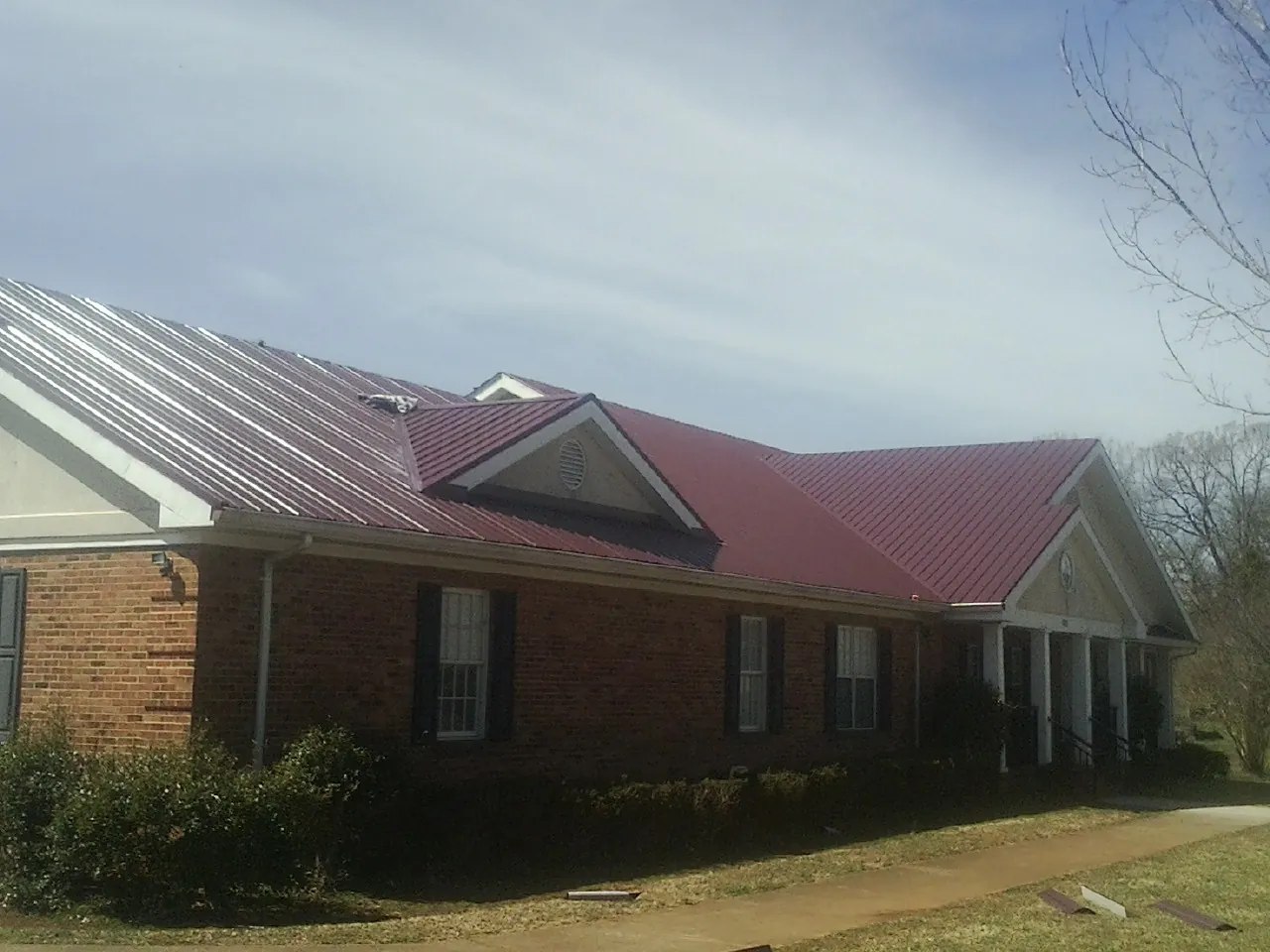 Red metal roof with gabled entries on a long brick building, from a Hail Damage Roof Repair job in San Anselmo