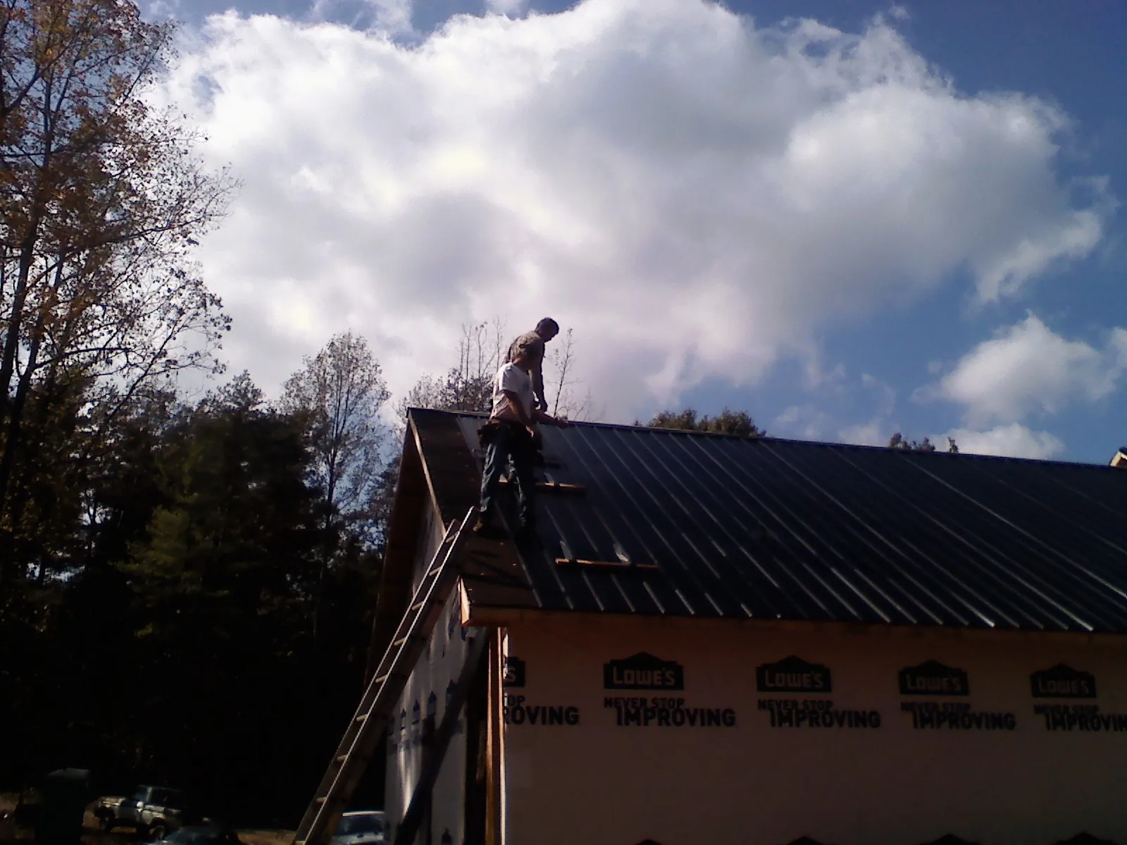 Roofer fastening dark metal panels high against a cloudy sky, from a Roof Inspection job in San Anselmo