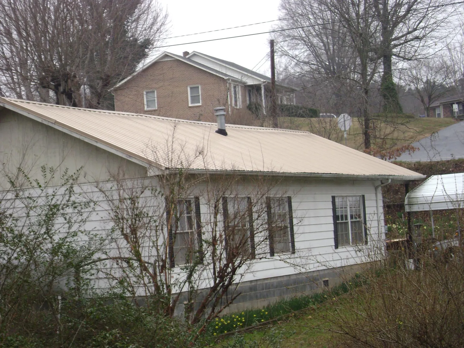Tan metal roof on a white sided house set into a hillside — Commercial Roofing by Roofing Brothers in San Anselmo